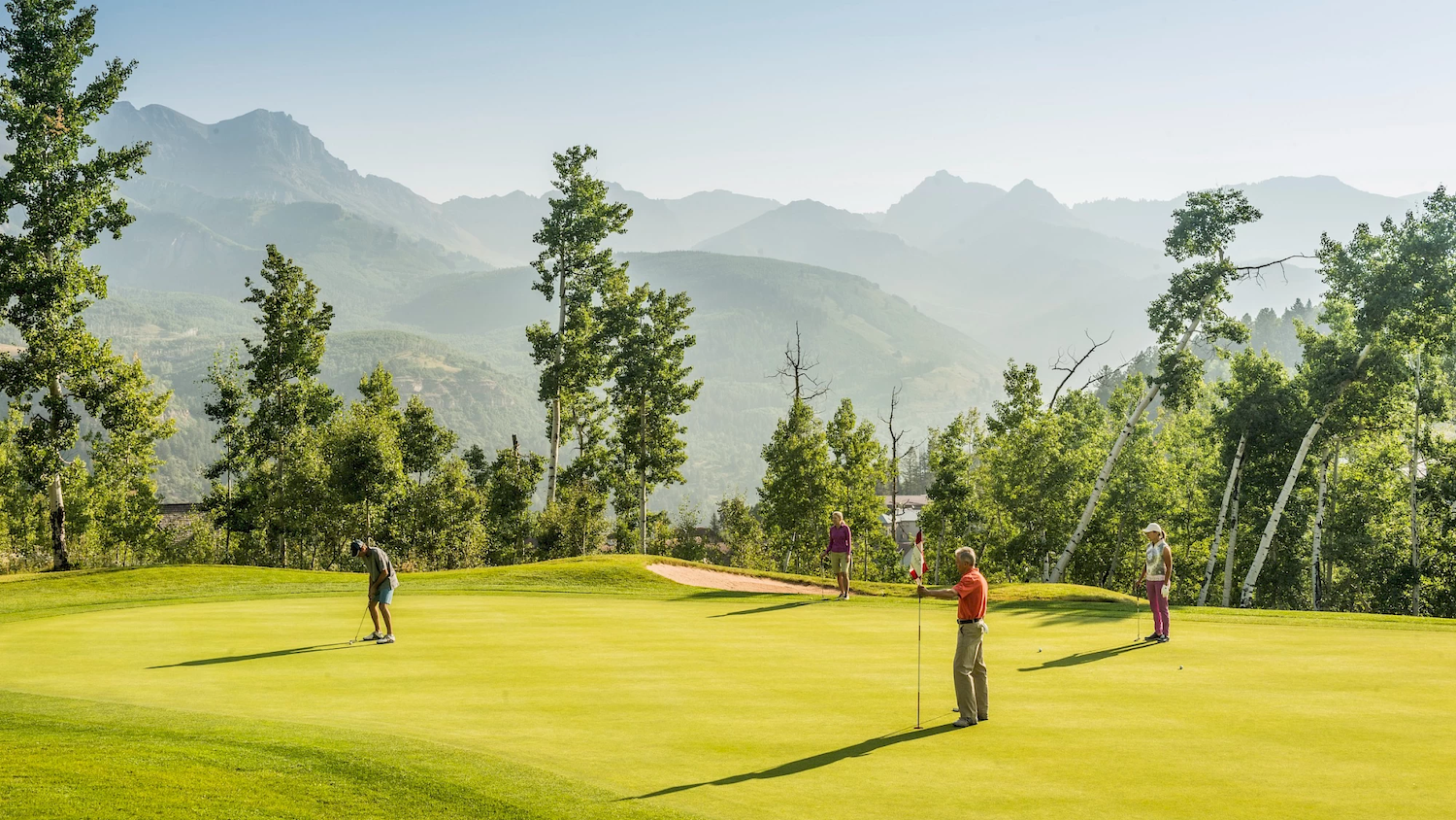 Members putting on a manicured mountain golf green framed by aspens and distant peaks
