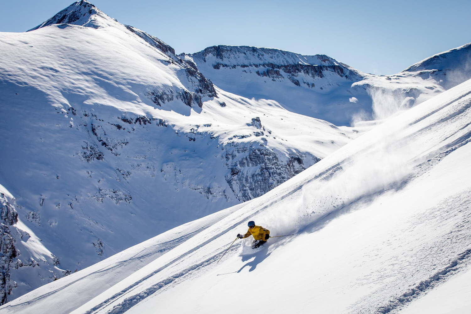 A skier carving through deep untouched powder beneath high alpine peaks